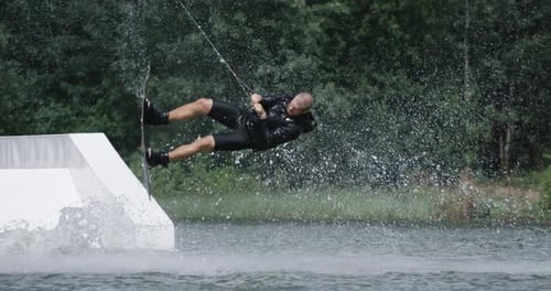 Wakeboarden in einem See in Waldnähe, Sportler surft auf dem Wasser, Fahrt auf einem Wakeboardboard