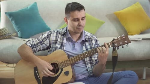 Man Playing Acoustic Guitar and Writing Song at Home