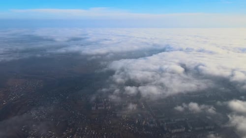 Aerial View From High Altitude of Distant City Covered with Puffy Cumulus Clouds Flying By Before