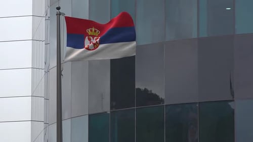 Serbian Flag Waving on Flagpole Against Modern Building