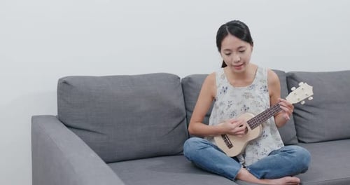 Woman play a song with ukulele at home