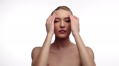 Beautiful Woman Rubs Forehead with Two Hands Rubbing Cosmetics White Background in Studio Front View