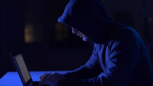 Person in Hood Using Laptop in Dark Room