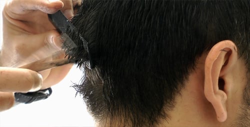 Close Up of Barber Cutting Dark Hair With Scissors