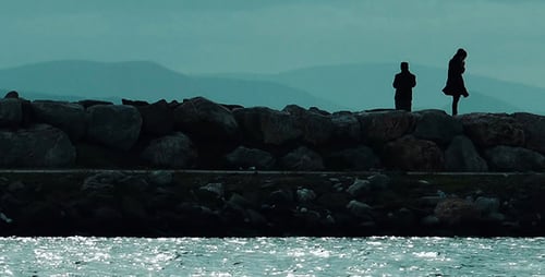 Silhouetted Figures Stand on Rocky Breakwater by Sea