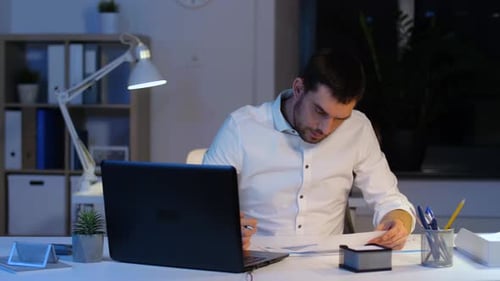 Geschäftsmann mit Papieren und Laptop bei Night Office 2