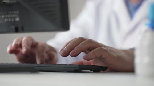 Nahaufnahme eines kaukasischen Mannes, des Arztes, der auf der Tastatur tippt und tippt, sitzt im Krankenhausbüro