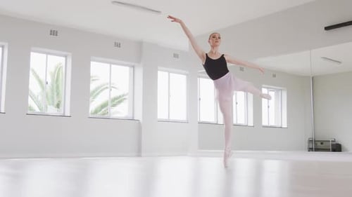 Caucasian female ballet dancer practicing ballet during a dance class in a bright studio