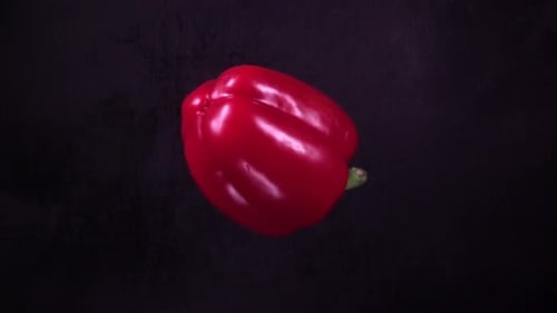Red Bell Pepper Falling on Black Surface and Slices