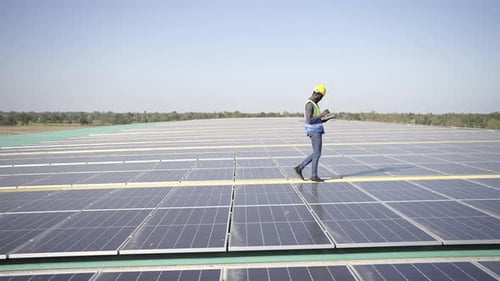 4K African man engineer using digital tablet maintaining solar cell panels on building rooftop.
