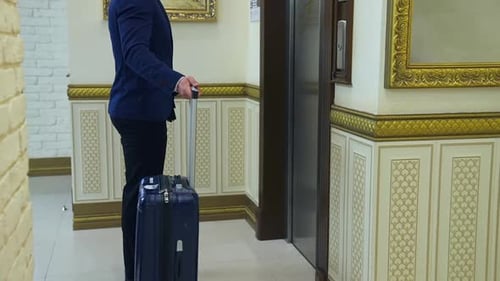 Man Awaits Elevator With Luggage in Hotel Lobby