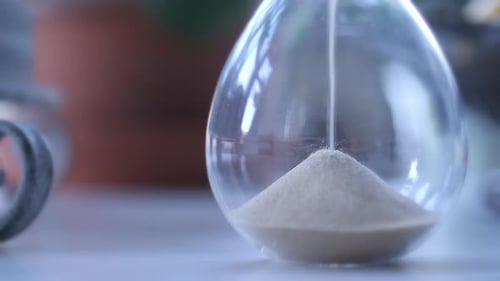 Sand Falling Through Clear Hourglass on White Table