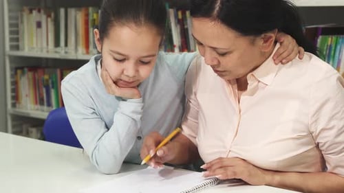 Girl Writing with Woman's Help in Library