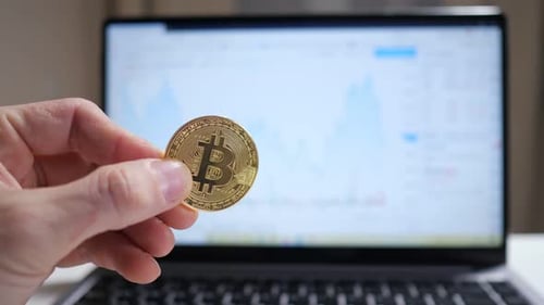 Holding Bitcoin Coin in Front of Computer