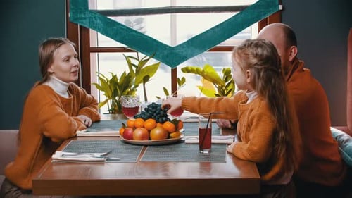 A Happy Family Sitting in the Hotel Restaurant - a Little Girl Eating Grapes and Feeding Her Parents