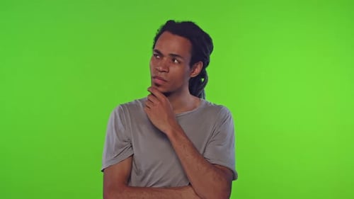 Young African American Man Thinks and Touches Chin Stands in Green Studio
