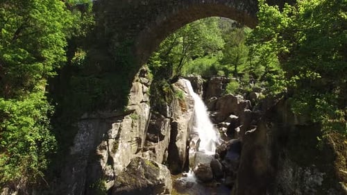 Majestic Waterfall Flowing Under Ancient Stone Bridge