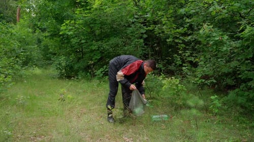 El hombre recoge basura en el bosque en una bolsa. Joven, atractivo hombre voluntario en uniforme