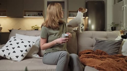 Woman Sits on Couch with Dog and Mug