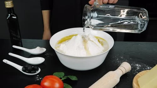 Koch bereitet Teig für Pizza zu. Hände gießen klares Wasser in eine Schüssel mit Mehl