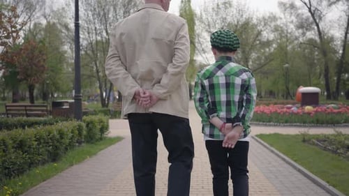 Portrait Grandfather and Grandson Walking in the Park with Their Backs To Camera