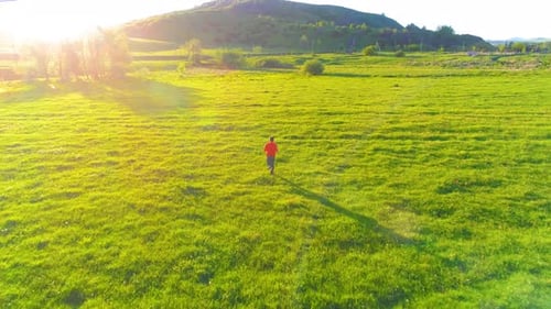 Flight Over Sport Man at Perfect Green Grass Meadow. Sunset in Mountain