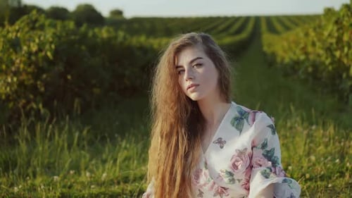 Young Lady Sitting Among Green Field and Dreaming When Looking at Sun Shining