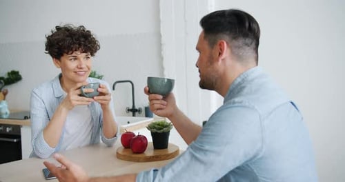 Happy Couple Chatting at Kitchen Table Over Coffee