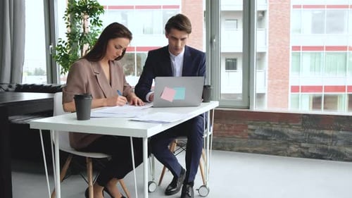 Young man and woman are working on a computer in a loft while discussing a project.