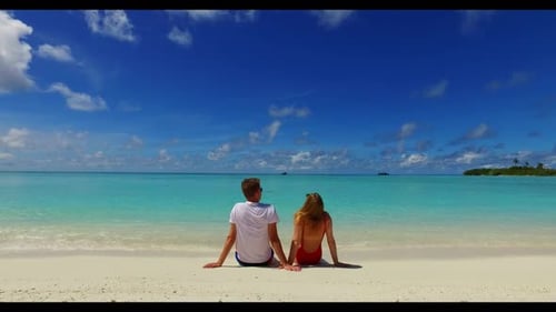 Romantic couple sunbathing on idyllic lagoon beach wildlife by blue lagoon and white sandy backgroun