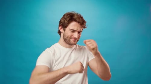 Happy Young Bearded Man Dancing with His Hands Against Blue Background