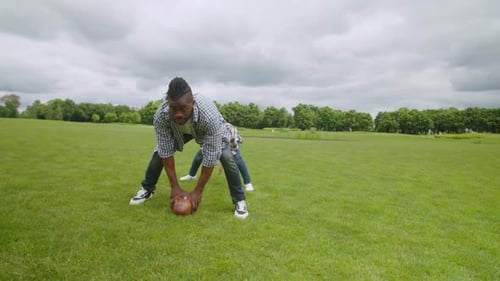 Man and Child Play Football in Grassy Field