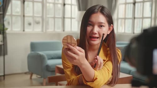 Mujer bloguera de belleza filmando un tutorial diario de rutina de maquillaje ante la cámara en un trípode