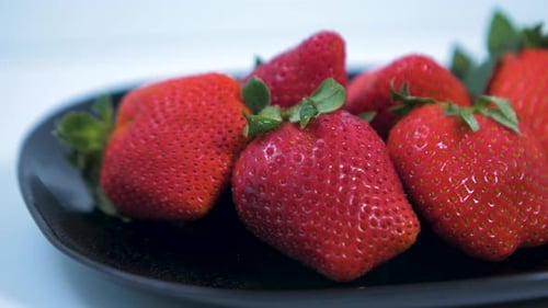 Fresh big red tasty ripe strawberries rotates slowly on a black plate on light blue background, heal