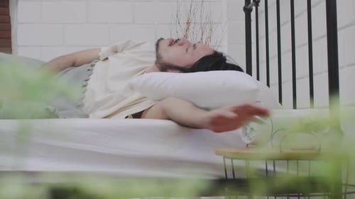 Man Lying in Bed Turns Off Alarm Clock