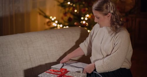 Woman Tying Ribbon on Christmas Presents in Cozy Home
