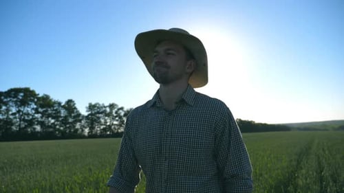 Happy Male Farmer in Hat Walking Over Green Wheat Field and Enjoying Nature