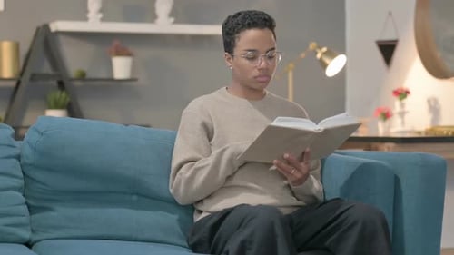 African Woman Reading Book While Sitting in Sofa