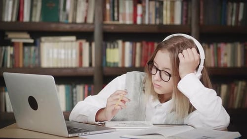 Teenage Girl Wearing Headphones and Glasses Studying Online From Home with Distance Teacher