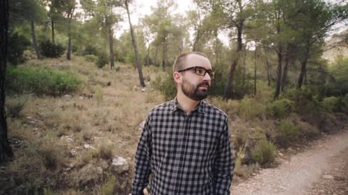 Junger kaukasischer Mann mit Sonnenbrille, der Bäume und Landschaft beim Gehen im Waldweg bewundert.