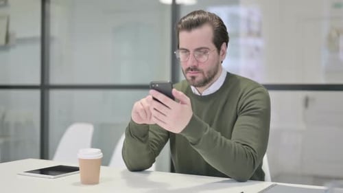 Attractive Young Businessman Using Smartphone in Office