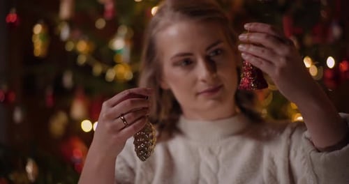 Woman Holds Christmas Ornaments in Front of Tree