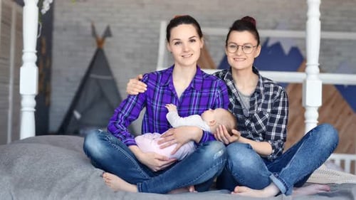 Two Mothers with Baby Sitting on Bed