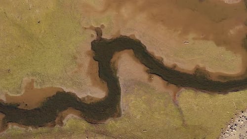 Luftaufnahme von oben nach unten auf einen kleinen Fluss, der an einem heißen Sommertag durch trockenes Land fließt.