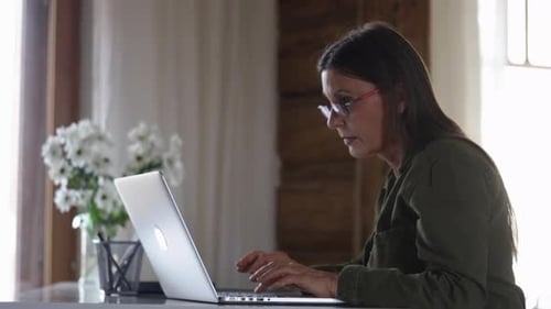 European Elderly Woman is Using Laptop for Remote Work Sitting at Table in Home Interior Spbi