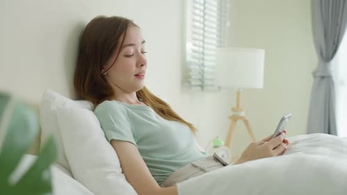 Woman Uses Smartphone Lying in Bright Bed