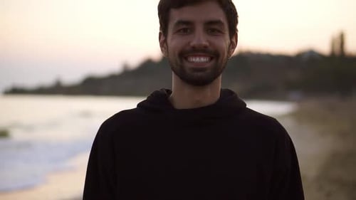 Portrait of a Charming Man Smiling Confident on Calm Seaside Beach Wearing Black Hoodie