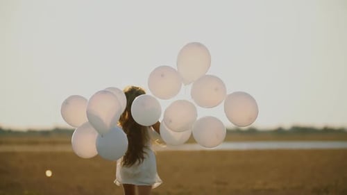 Child Walks With White Balloons in Golden Field