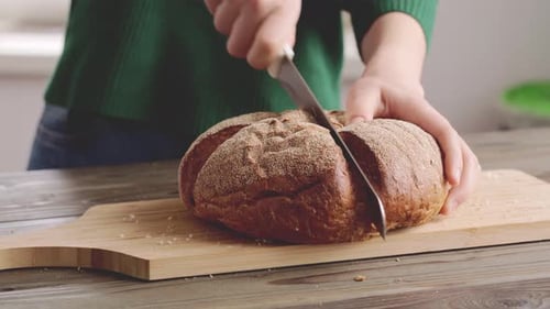 Hands of a Woman Cutting Bread Loaf on Wooden Cutting Board
