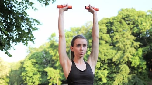 Woman Lifting Orange Dumbbells in a Green Park